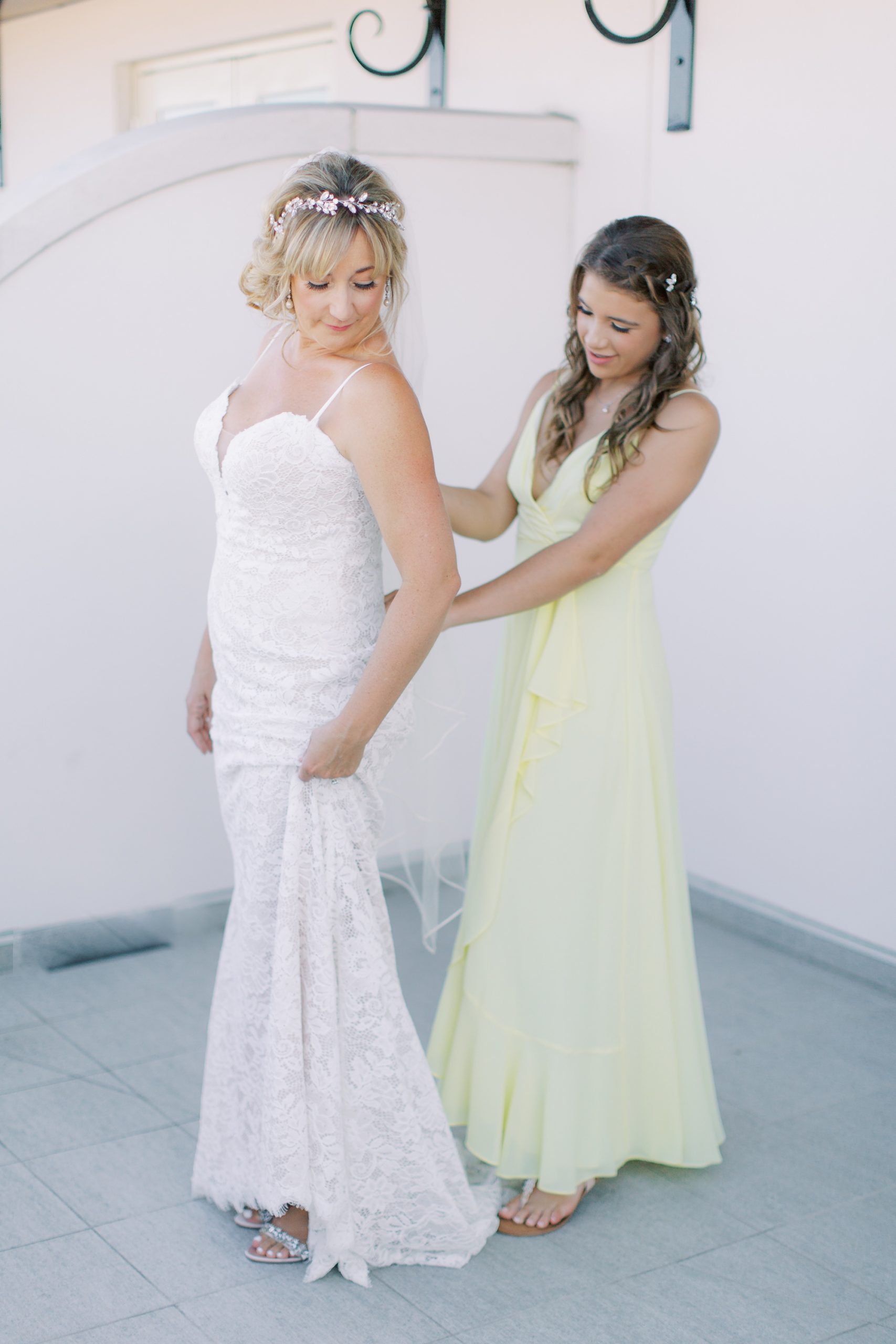 daughter in yellow gown helps mother into wedding dress