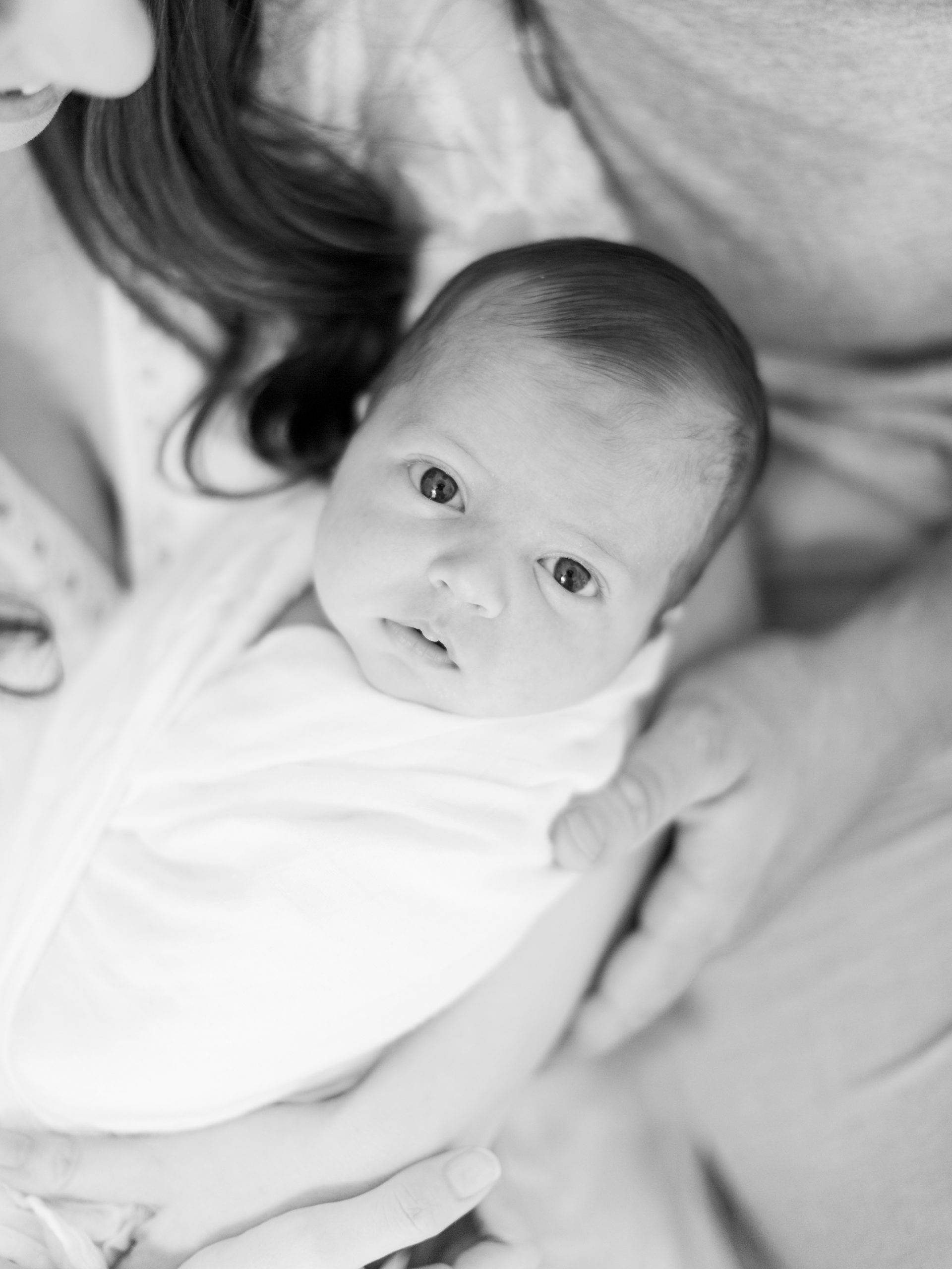 baby boy in white swaddle looks at photographer