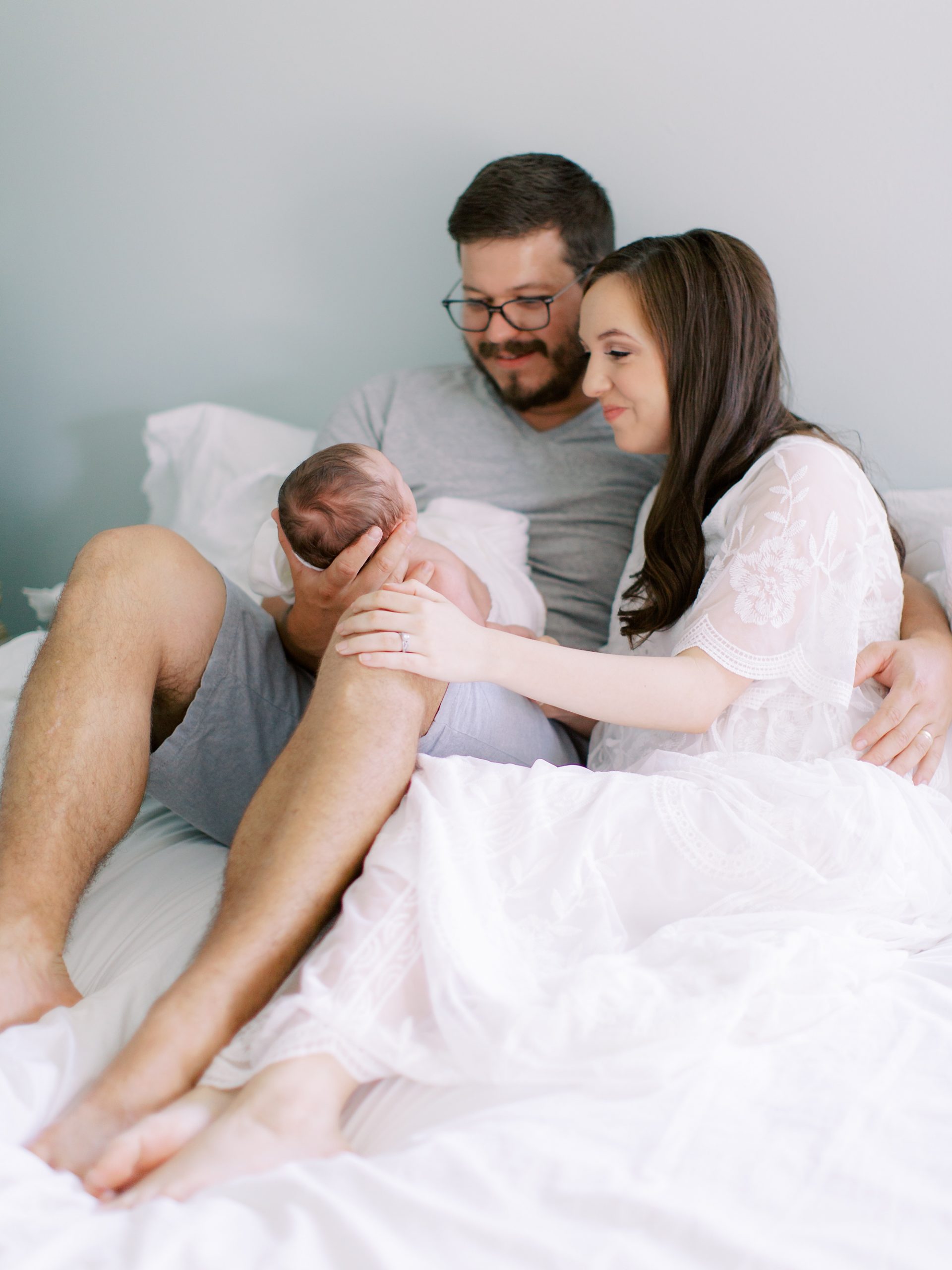 new parents sit with baby boy on bed during Charlotte newborn session