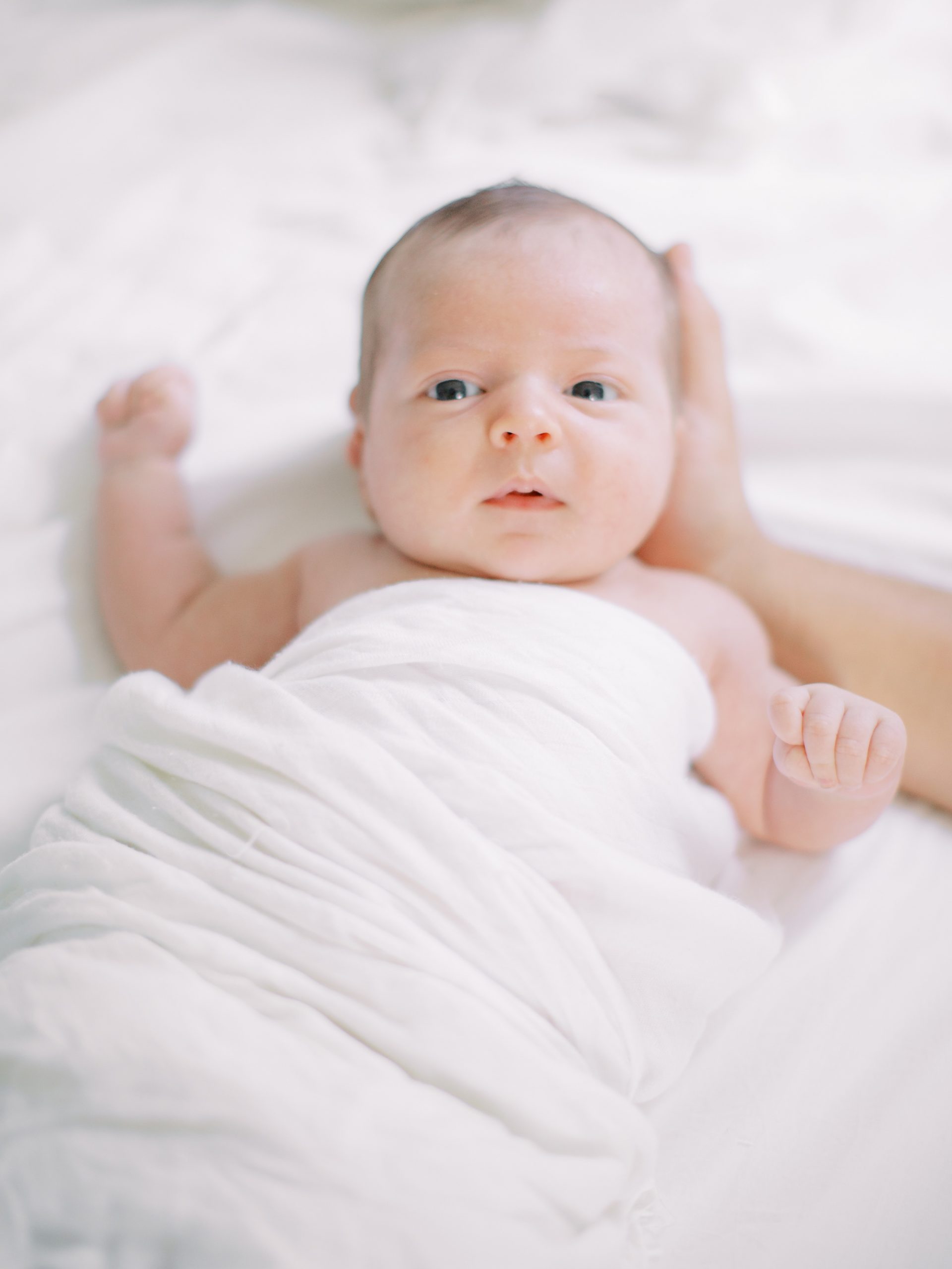 baby boy in white swaddle lays on bed