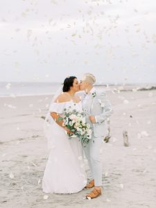 couple kisses while flower petals thrown around them
