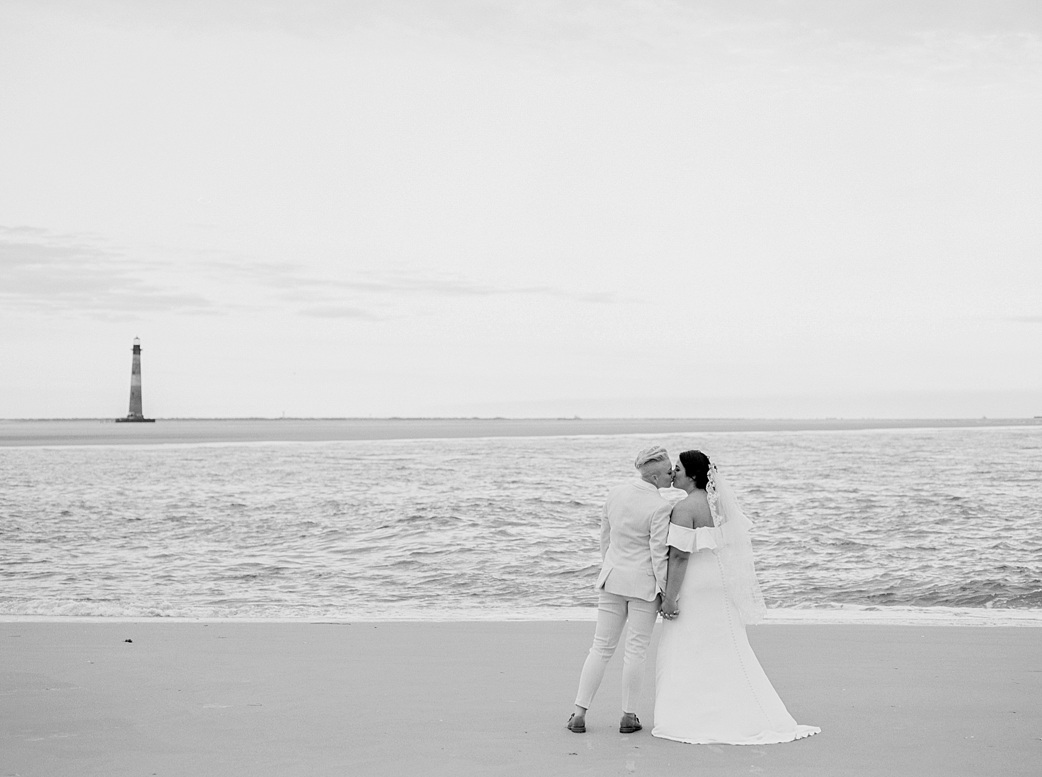 couple kisses on beach with lighthouse in distance