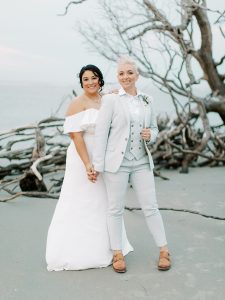 married couple poses by driftwood on Charleston beach