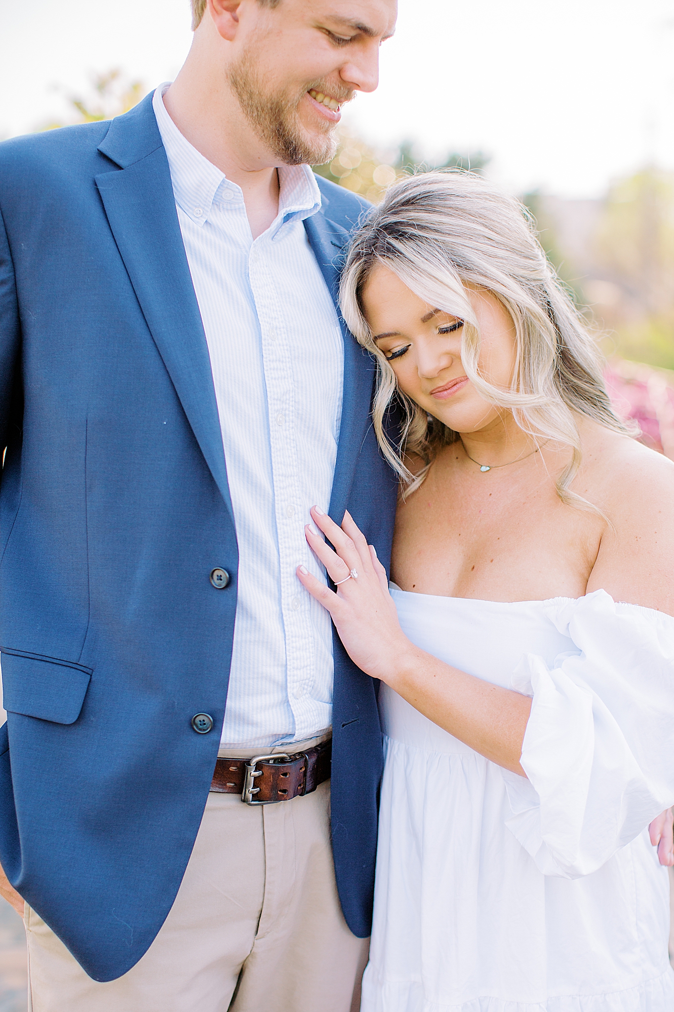 bride leans against groom's chest in blue suit jacket during Midtown Park engagement session
