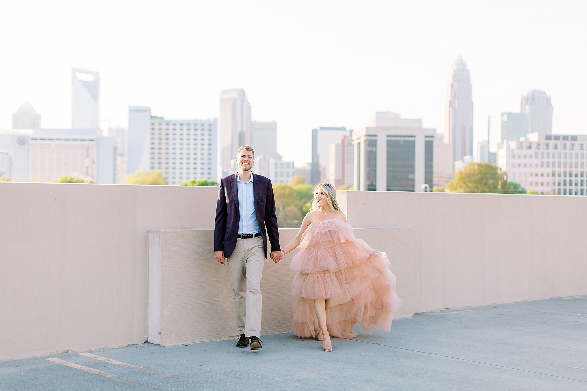 bride and groom walk with Charlotte skyline in backdrop