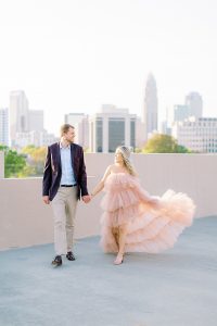 bride walks on rooftop twirling Untamed Petals during Uptown Charlotte engagement photos