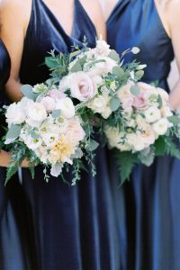 bridesmaids in navy blue dresses hold bouquets of white and pink florals
