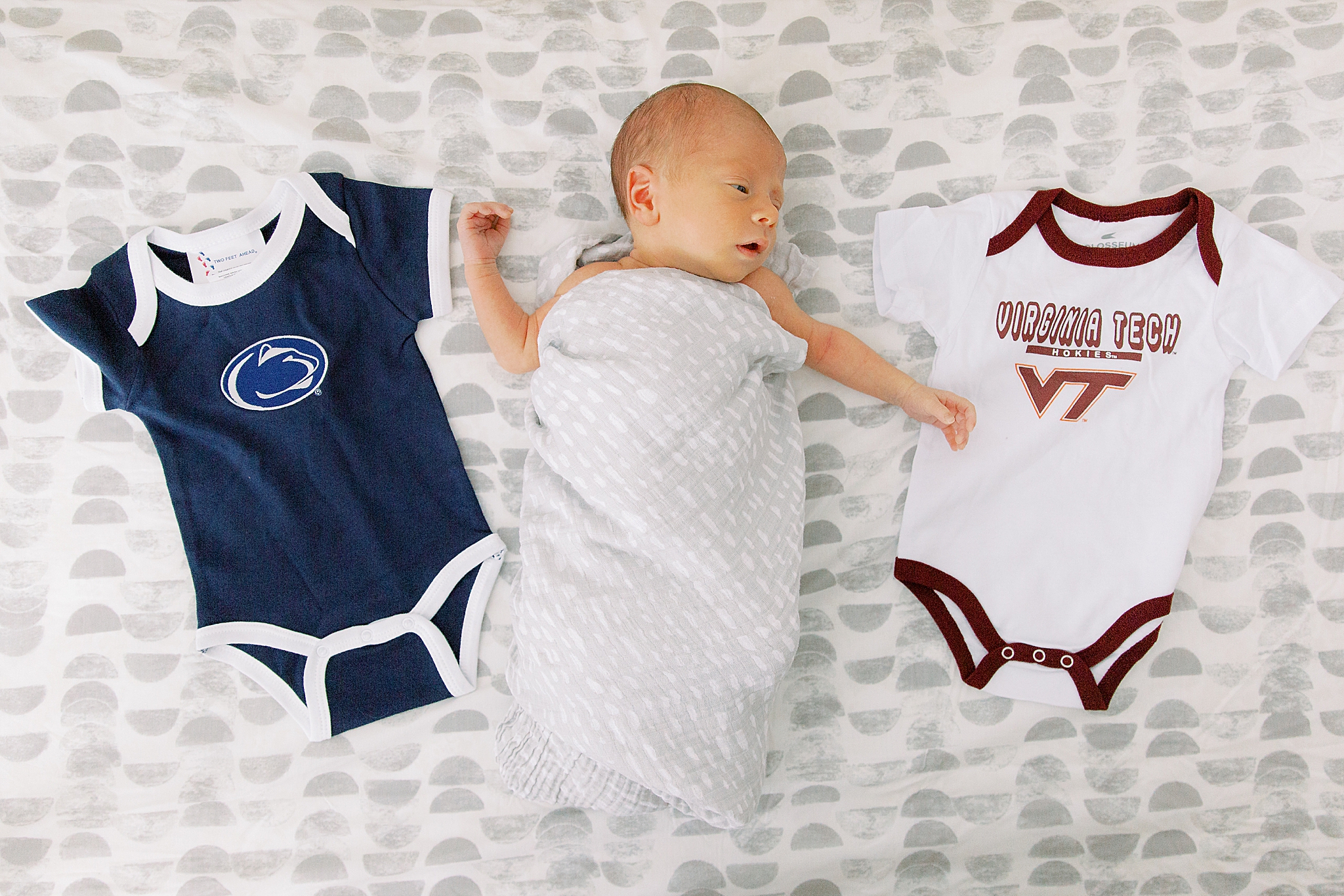 baby lays in nursery between VT and Penn State onesies