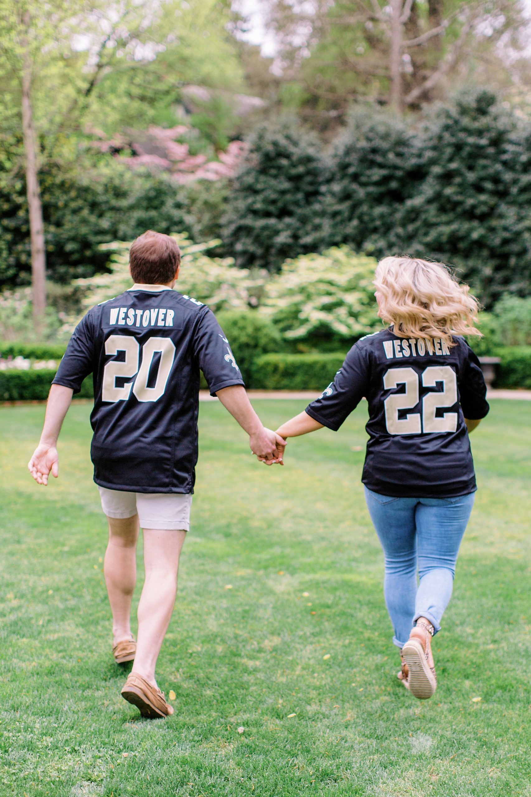 engaged couple walks through field wearing custom jerseys