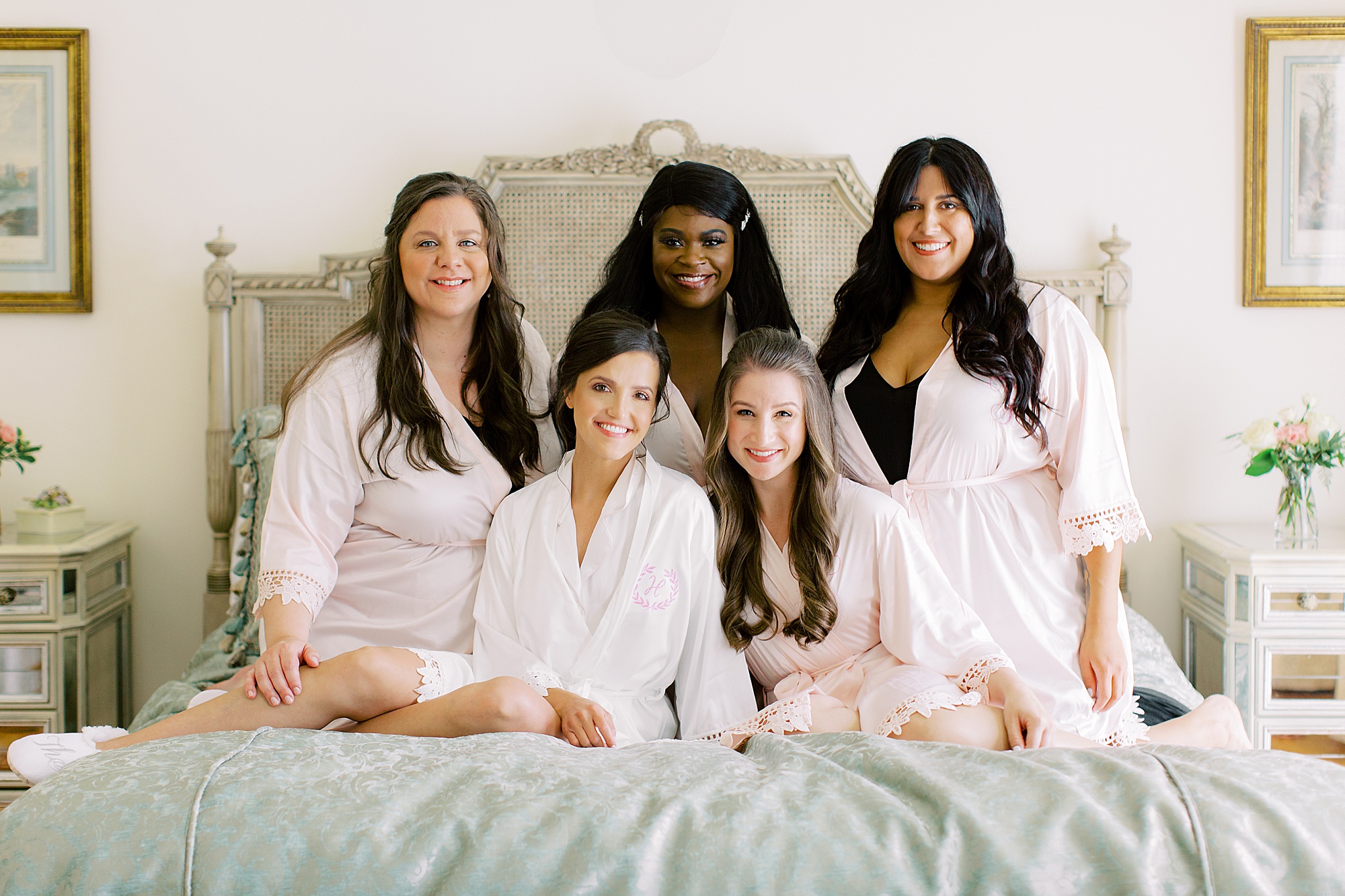 bride and bridesmaids sit on bed before Ballantyne Country Club wedding