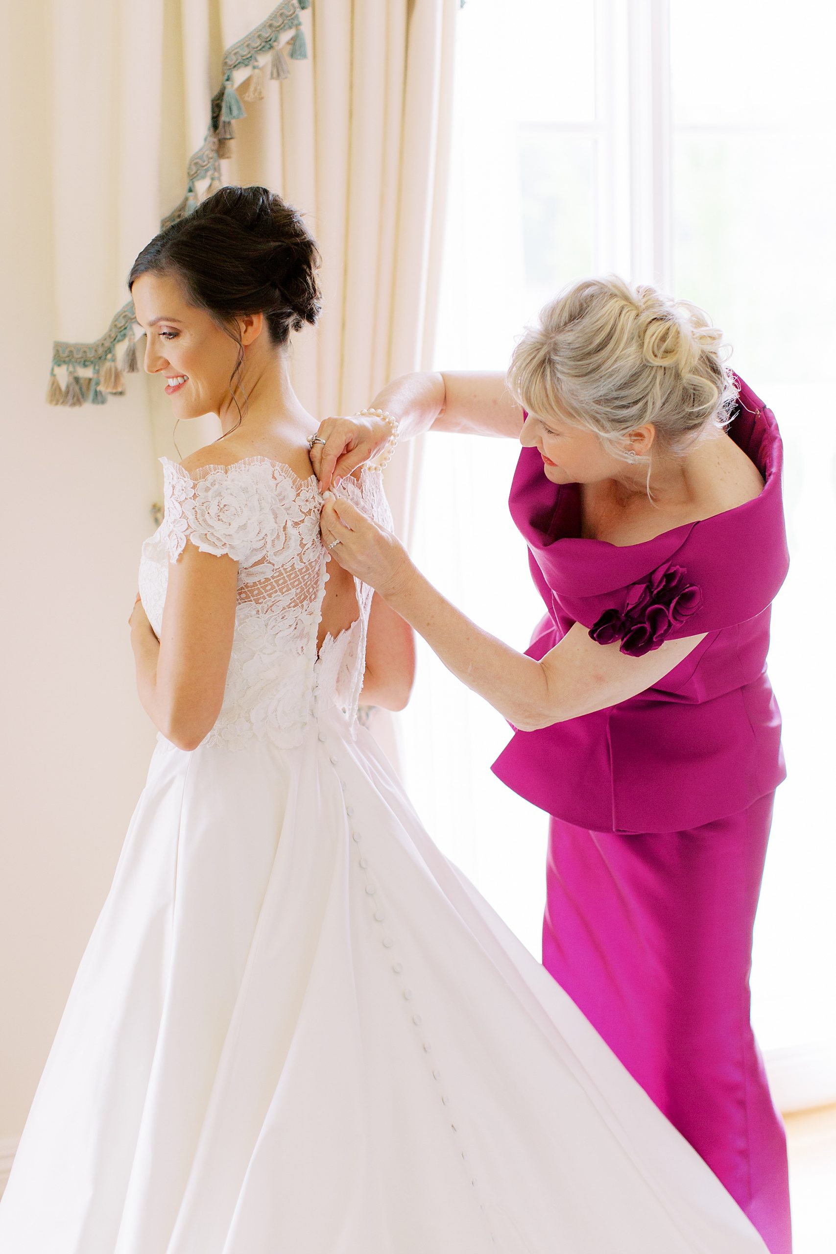 mother of the bride helps bride with wedding gown