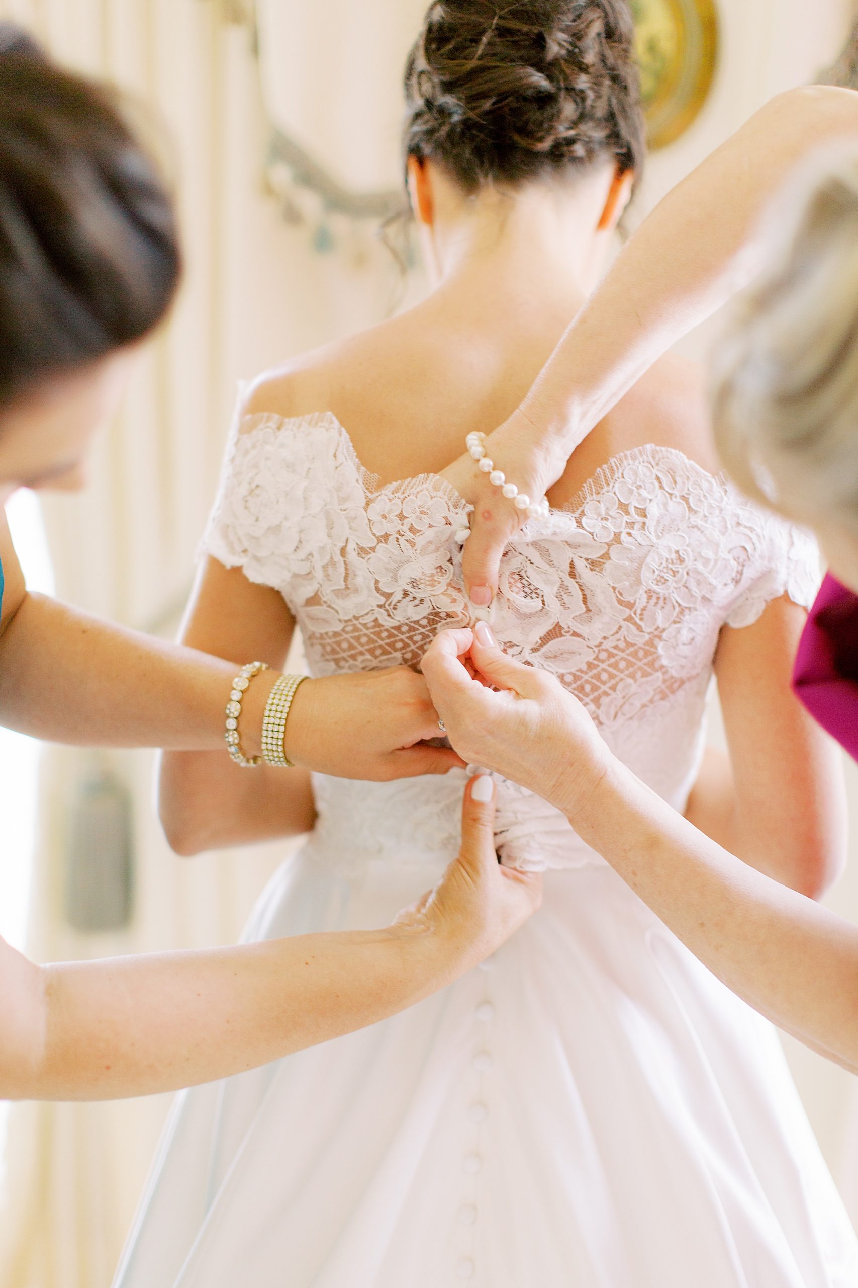 bridesmaid and mother help bride into wedding gown