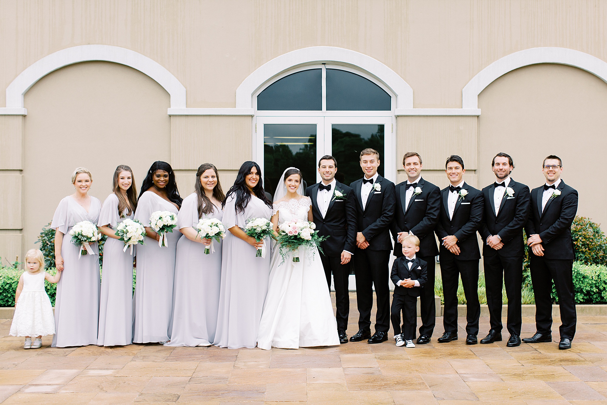 wedding party in pale grey gowns and classic tuxes pose with newlyweds