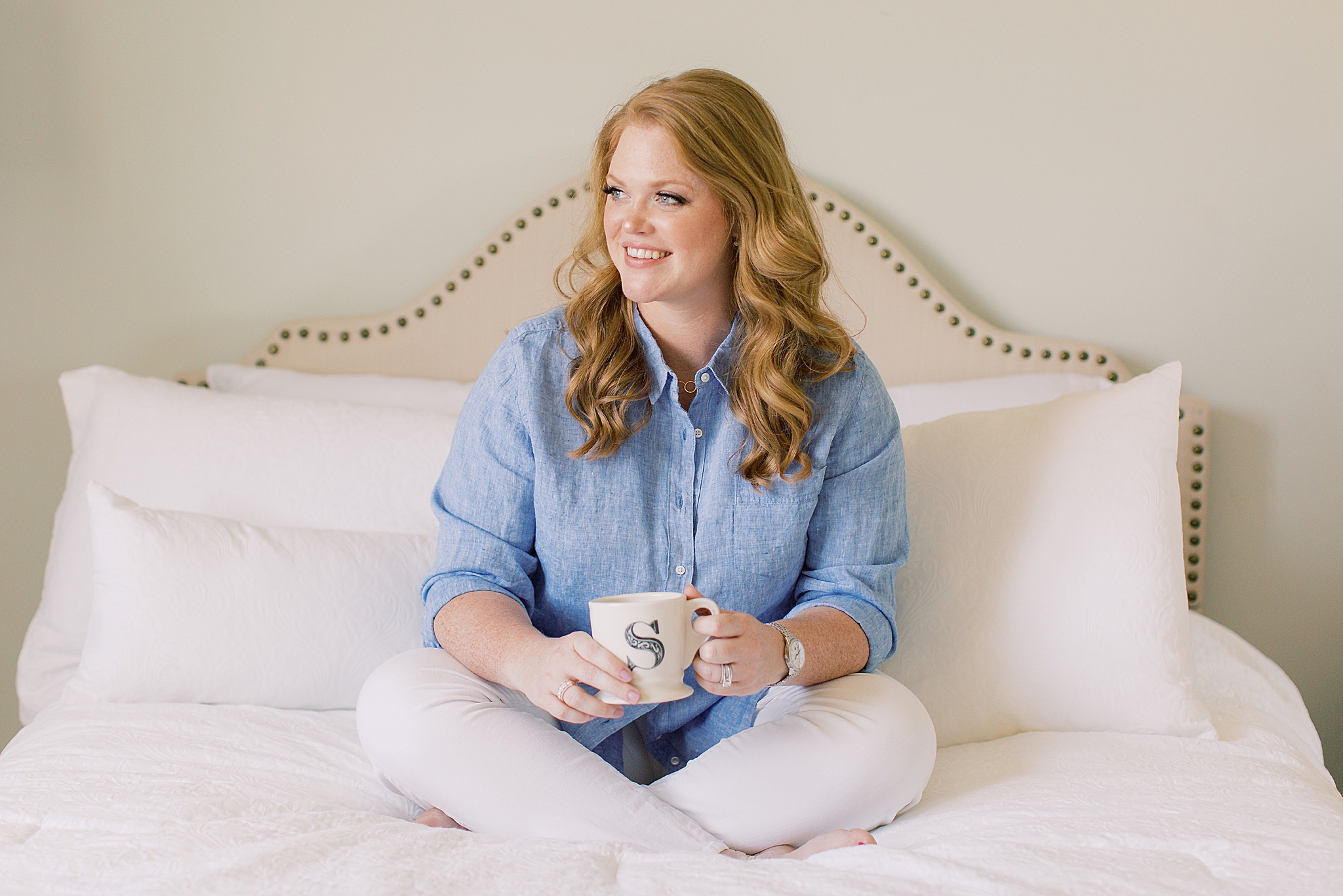 business owner sits on bed in blue shirt with coffee mug