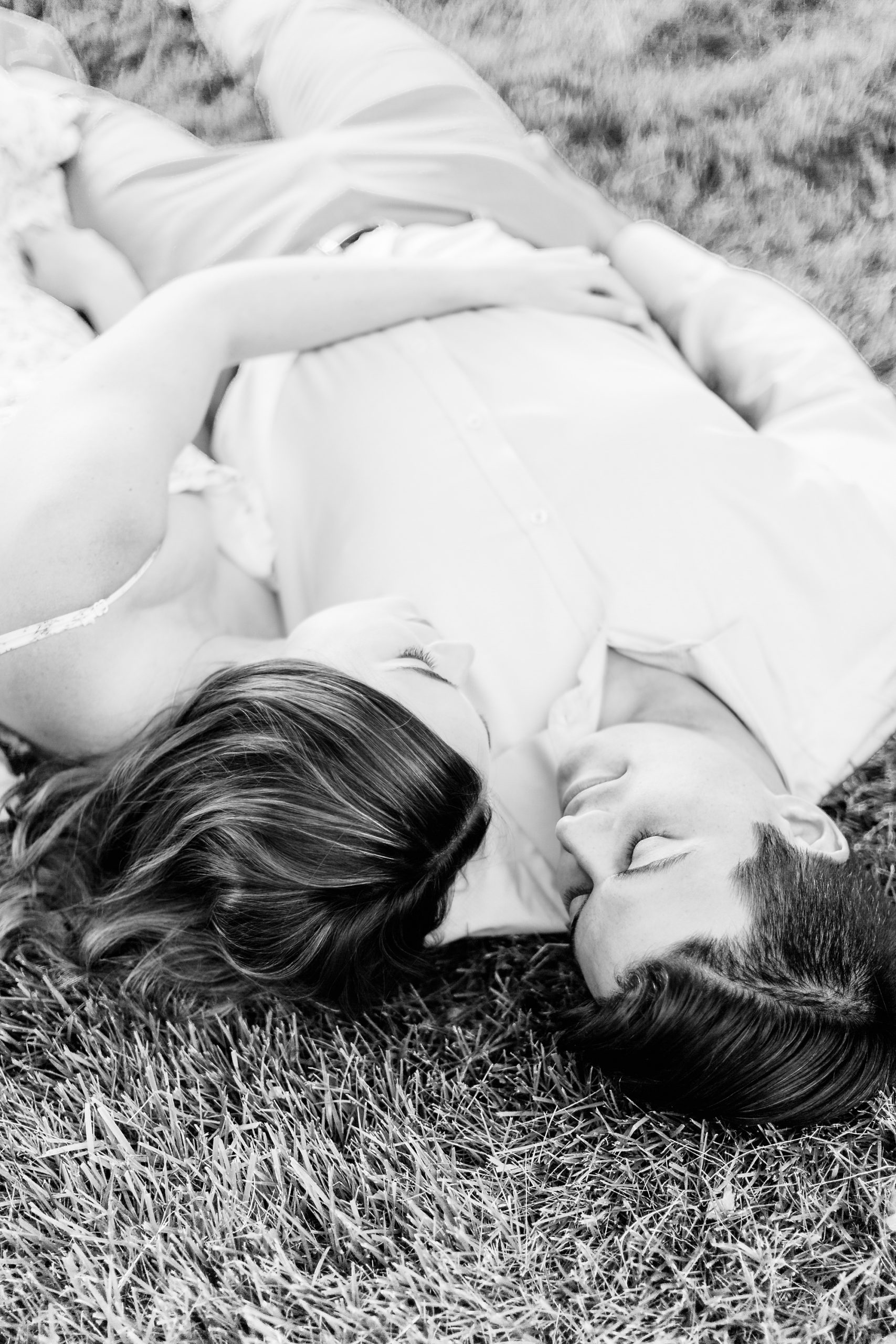 engaged couple lays in grass looking at each other