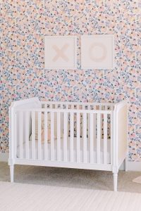 crib sits facing floral wallpaper