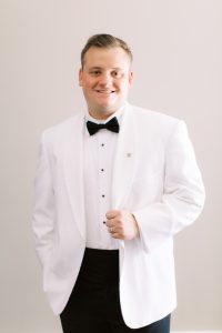 groom in classic white tux holds lapel
