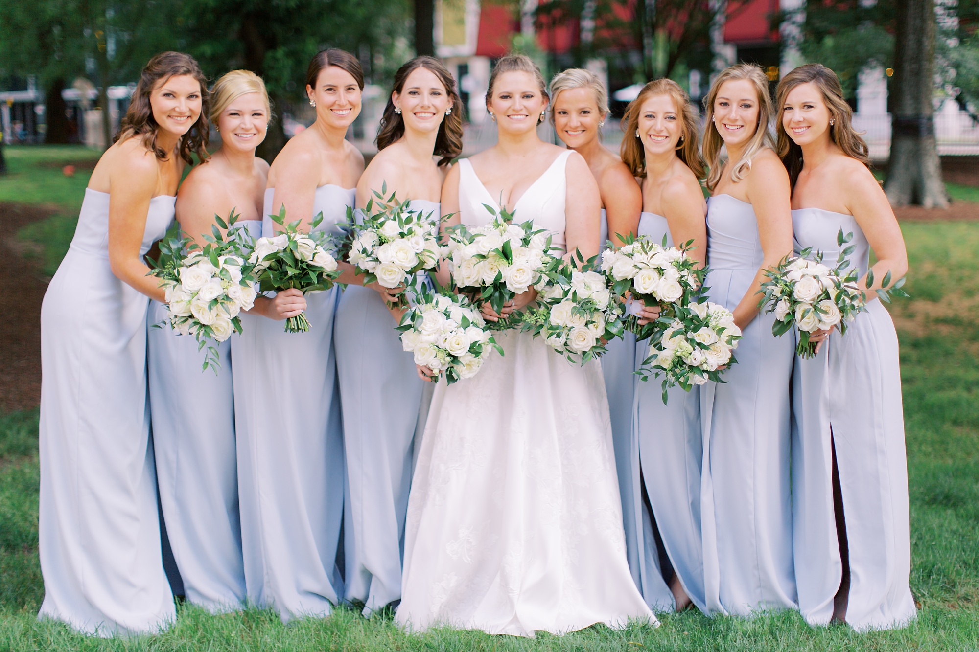 bride holds bouquet of white flowers with bridesmaids in blue gowns