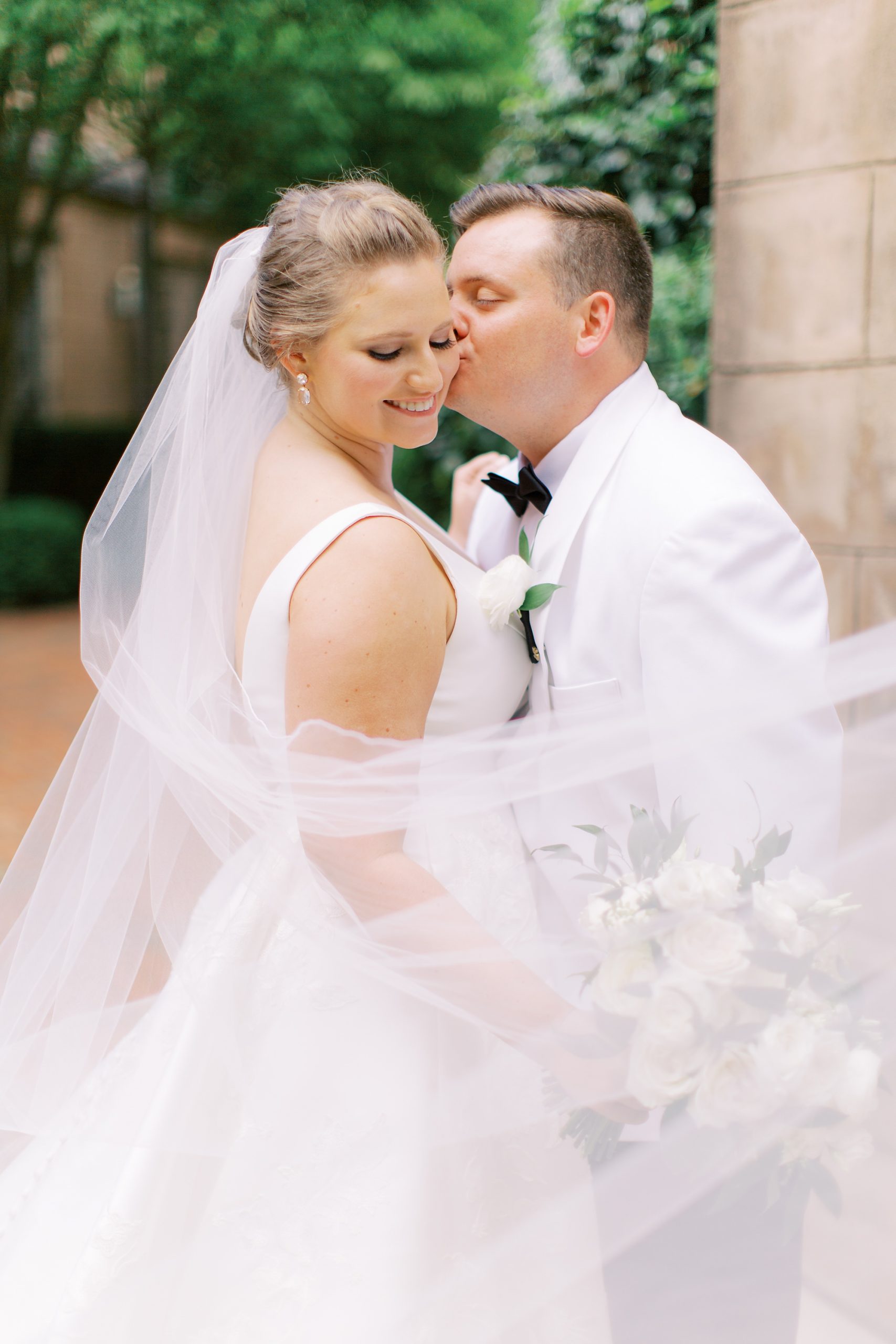 groom kisses bride's cheek with veil wrapped around them