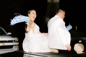 bride twirls pompoms on back of car during wedding exit