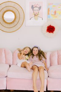 sisters sit on pink couch in Charlotte living room
