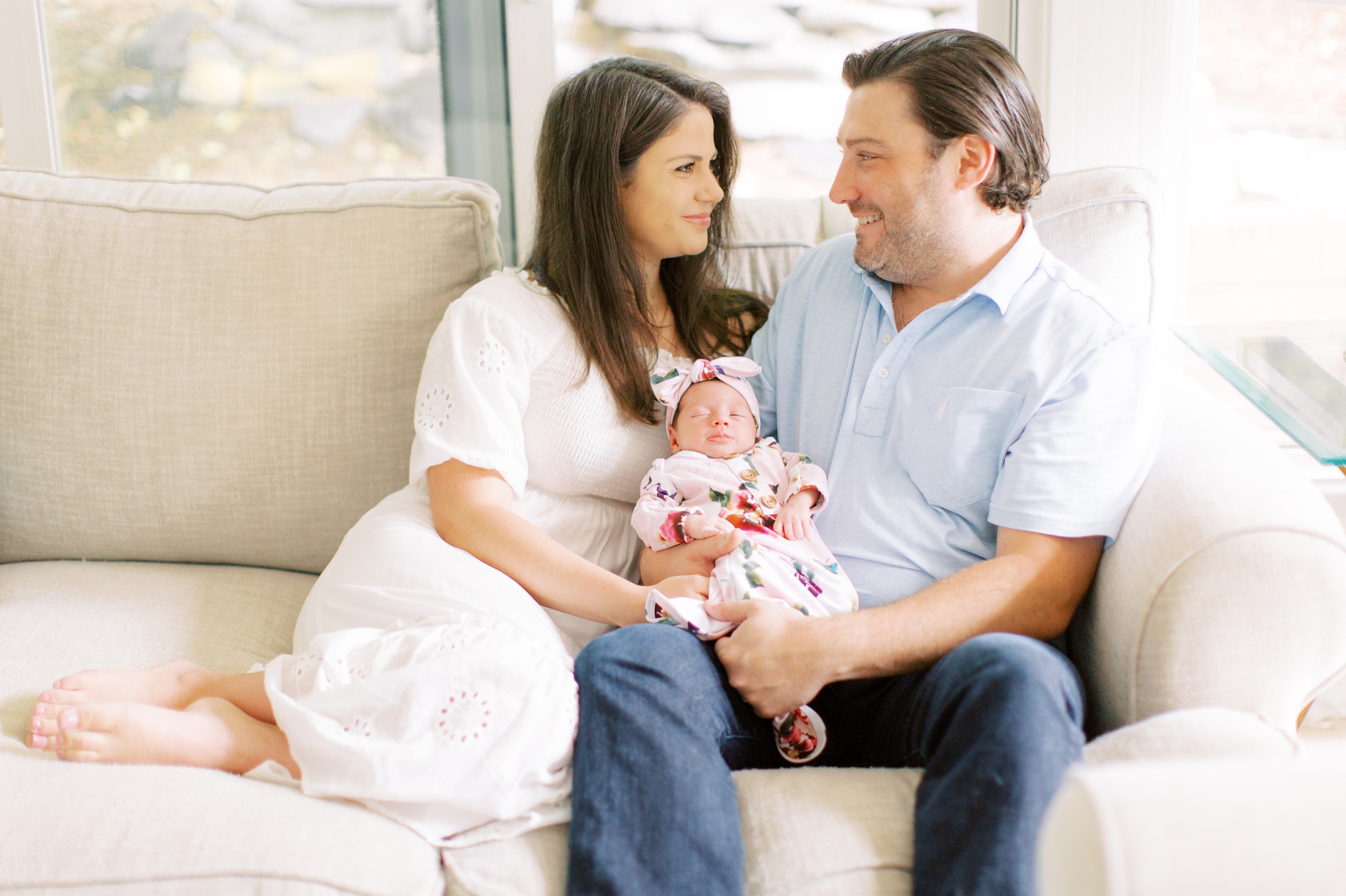 parents sit on couch hugging baby girl during newborn photos with Charlotte Newborn Photographer Demi Mabry