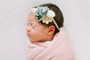 baby sleeps in pink wrap with floral headband during newborn photos