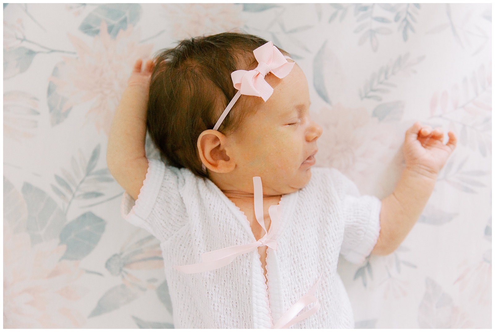 baby girl lays on floral sheet in knit shirt during Lifestyle Newborn Session in Charlotte