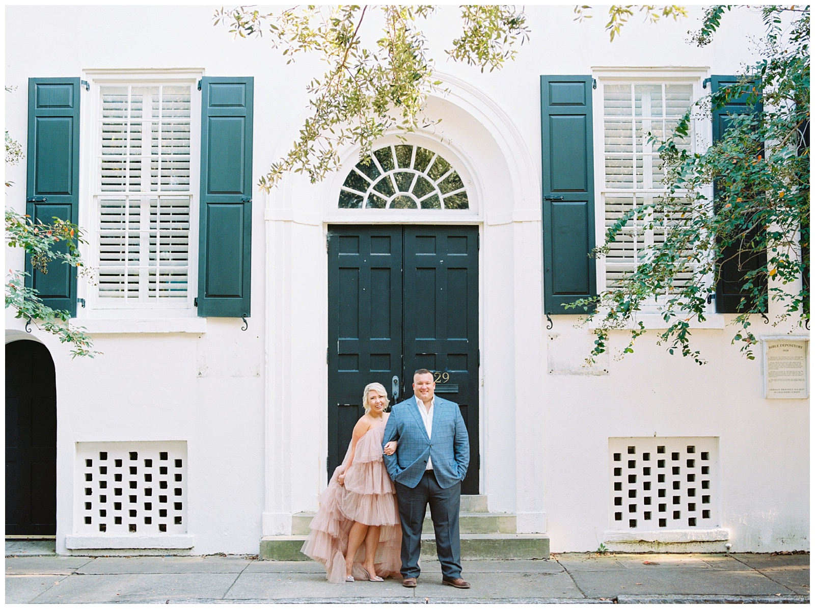 couple poses in front of historic home during Downtown Charleston engagement session