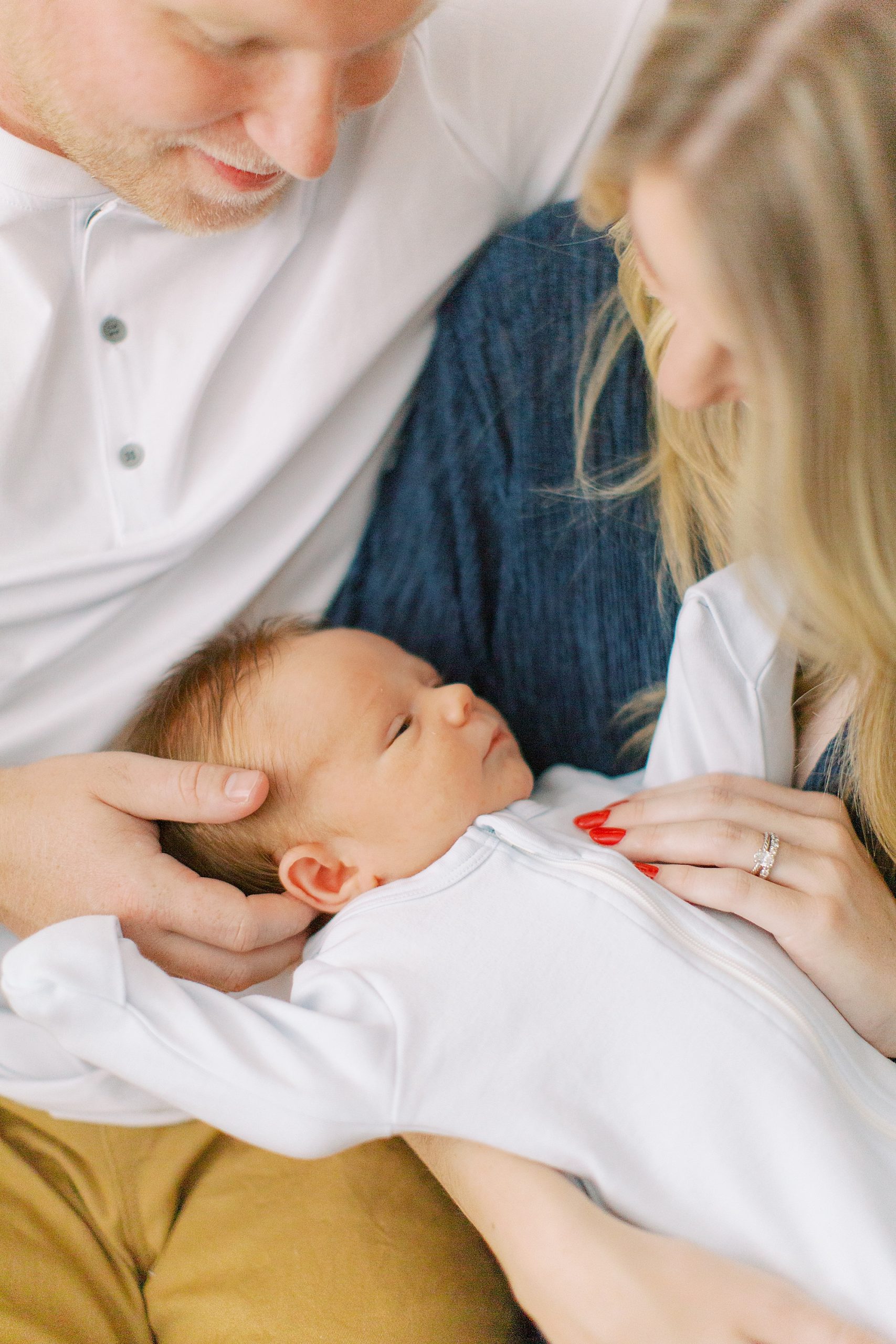 parents look at baby boy in white sleeper during newborn photos