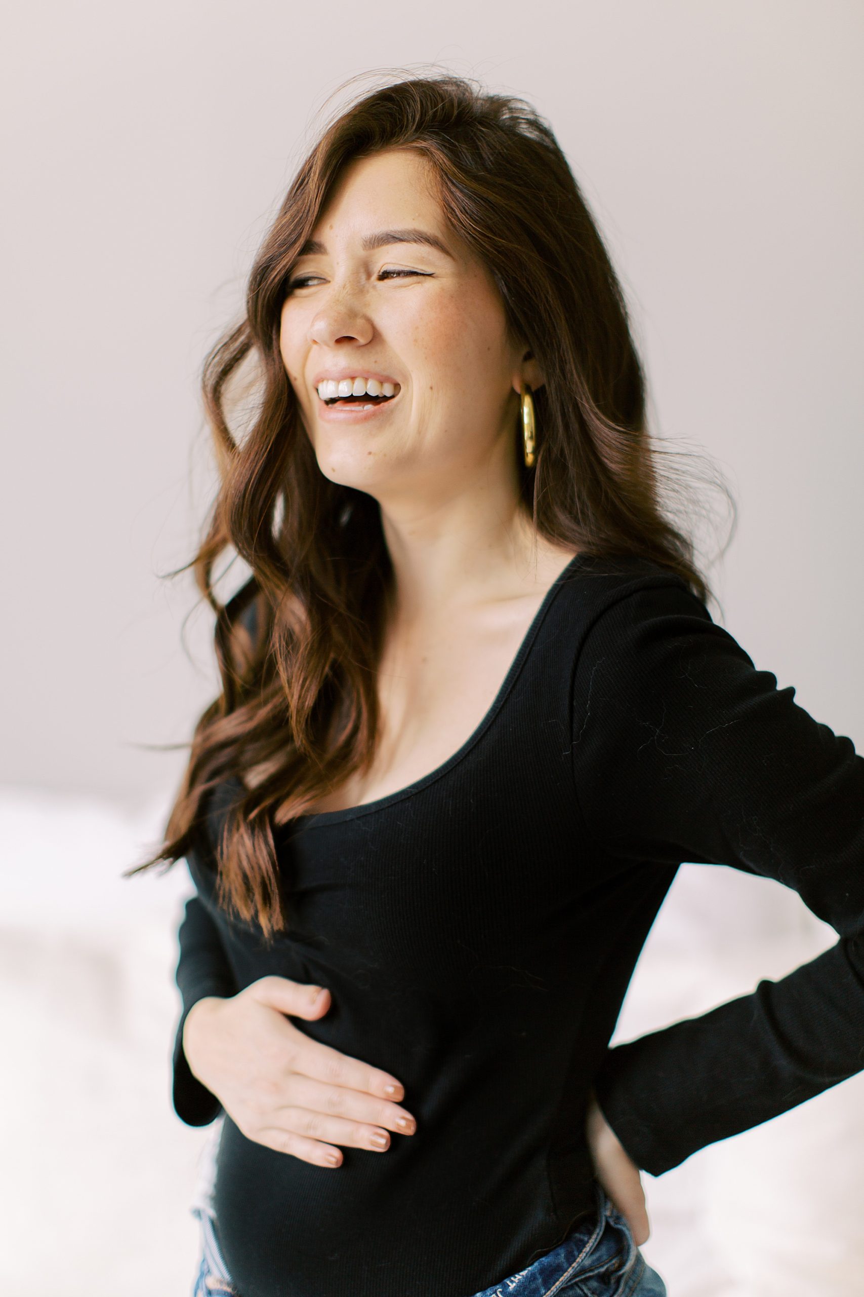 woman laughs holding belly during pregnancy announcement