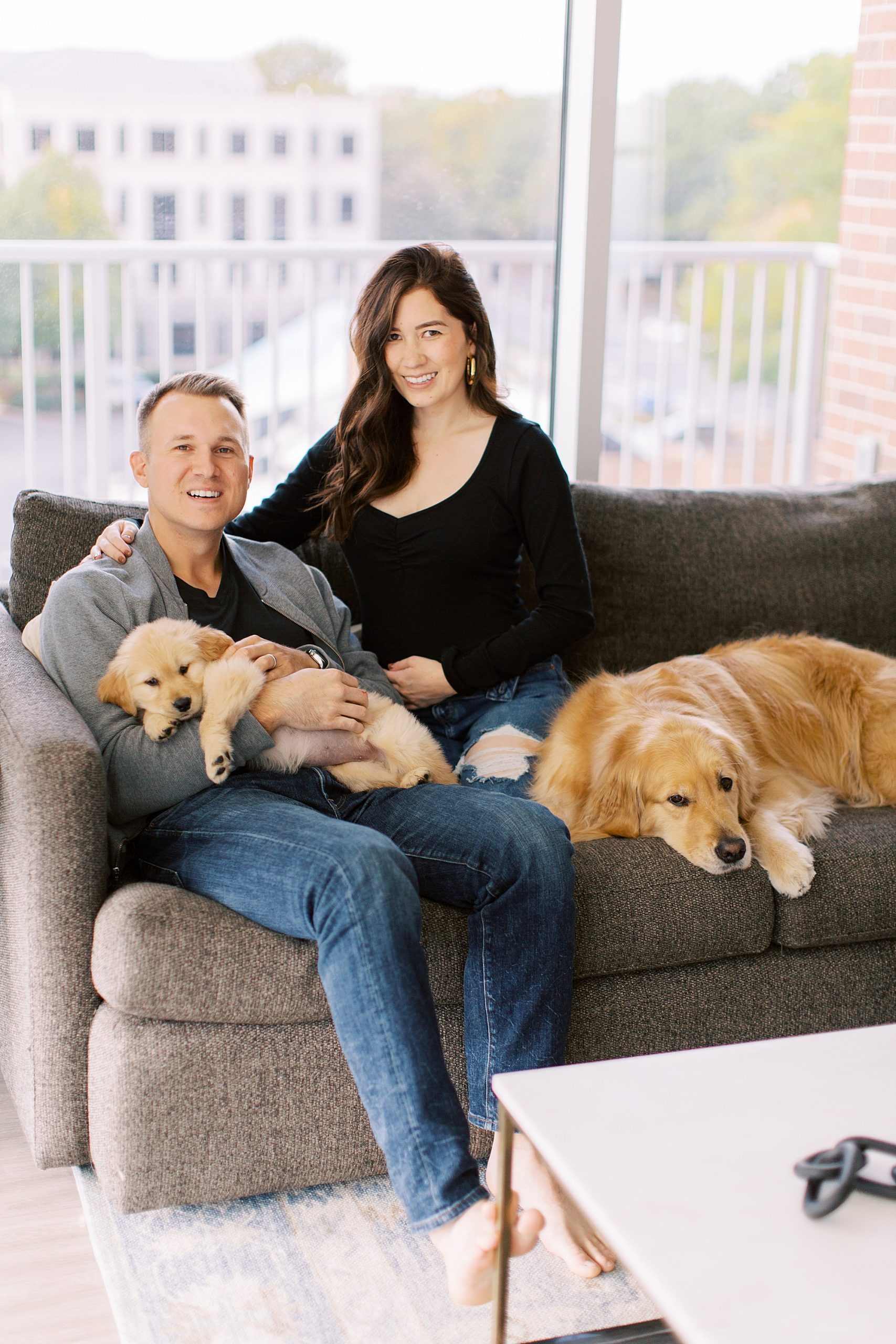 couple sits on sofa with golden retrievers