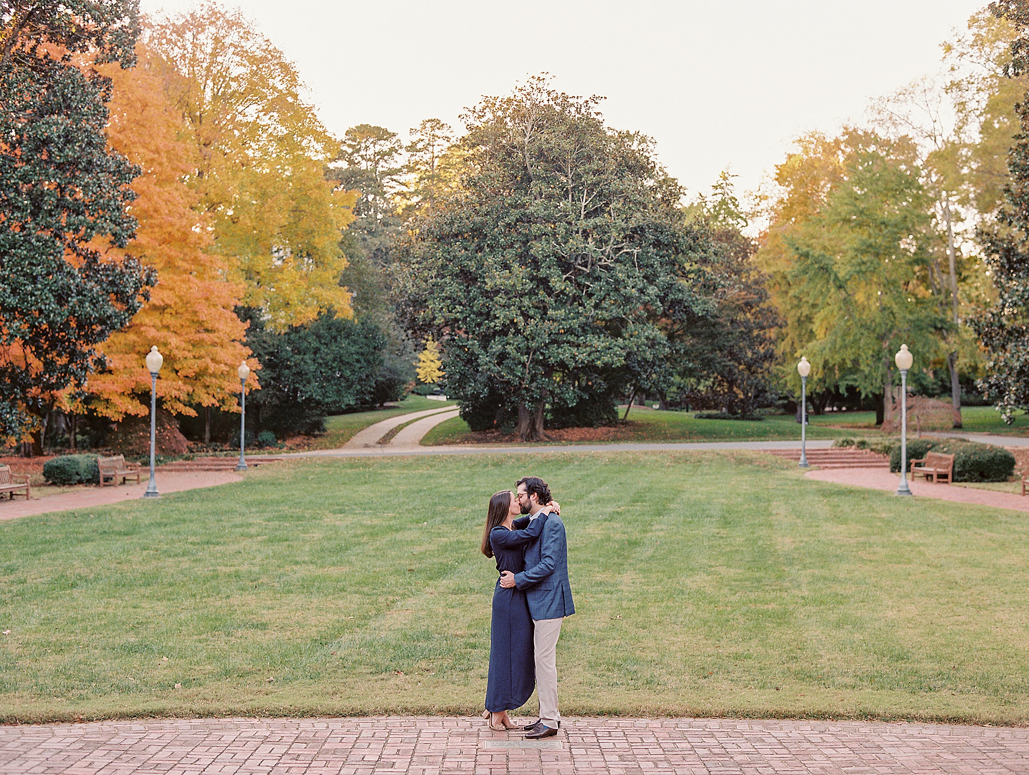 couple stands in front of lawn during fall Mint Museum engagement session