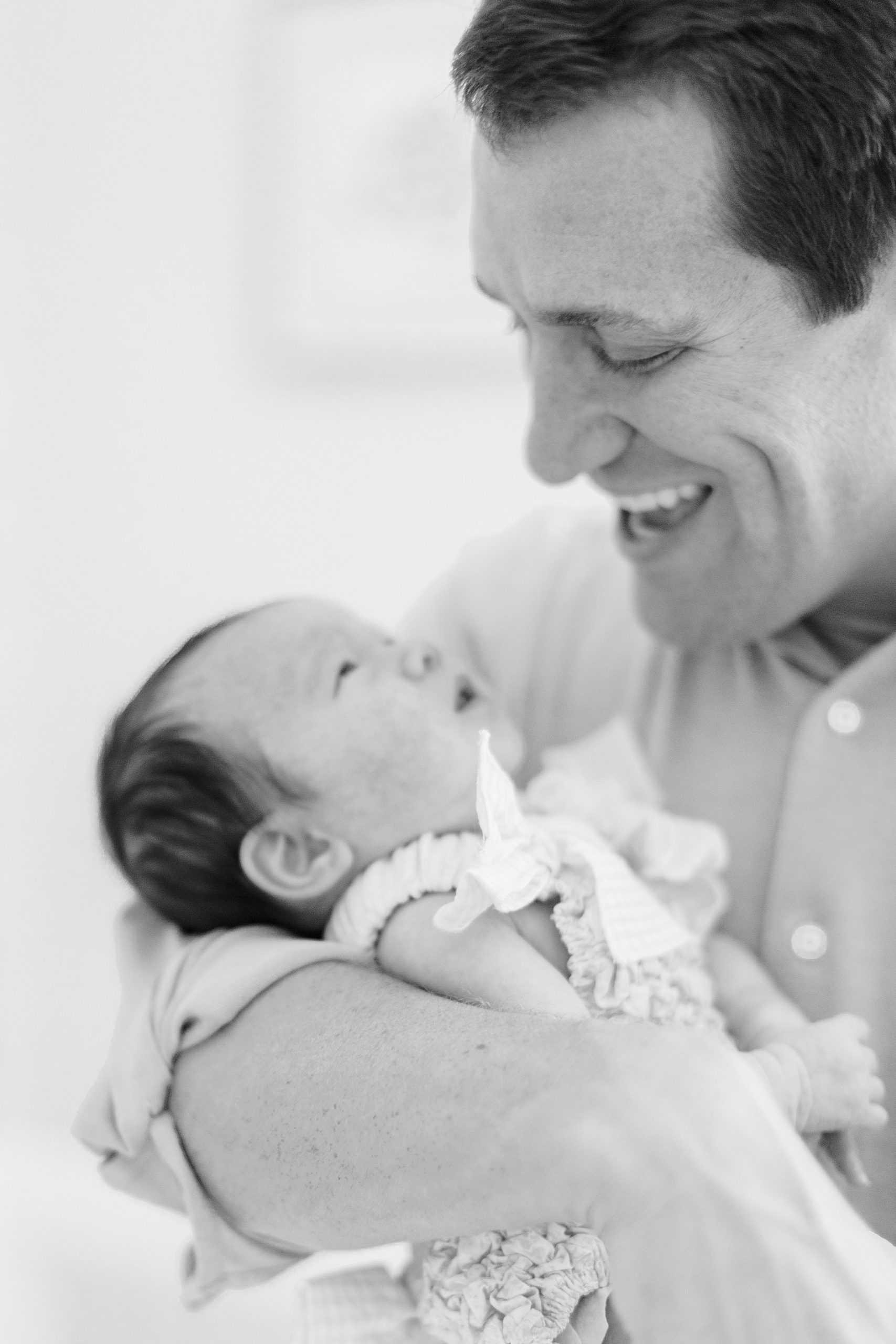 dad laughs looking at baby girl during newborn session at home