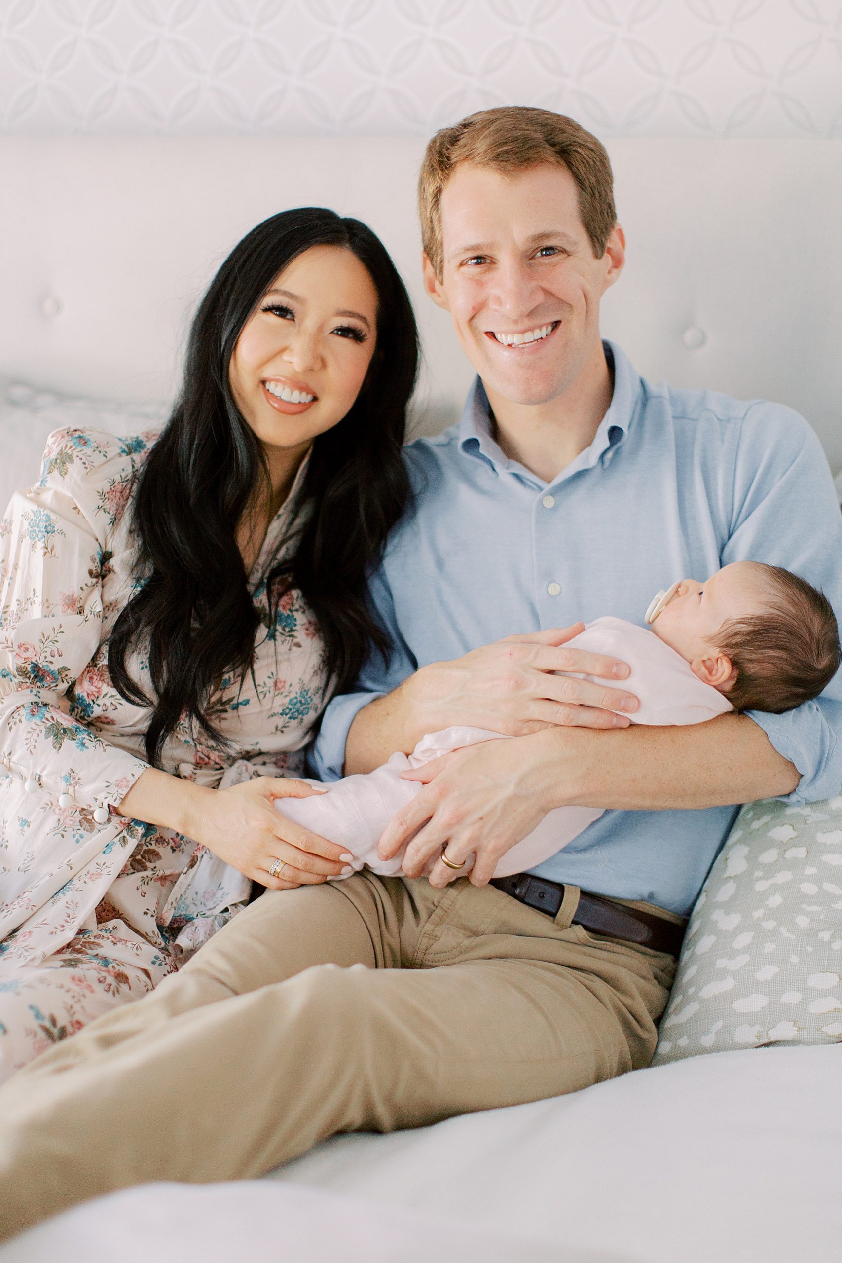 parents sit with new baby girl on couch during at-home newborn portraits