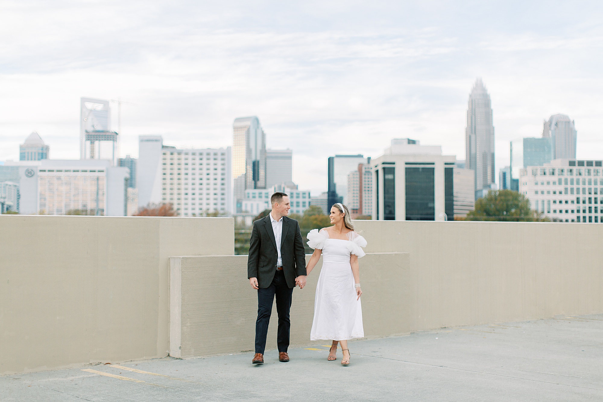 bride and groom hold hands with skyline behind them of Charlotte NC