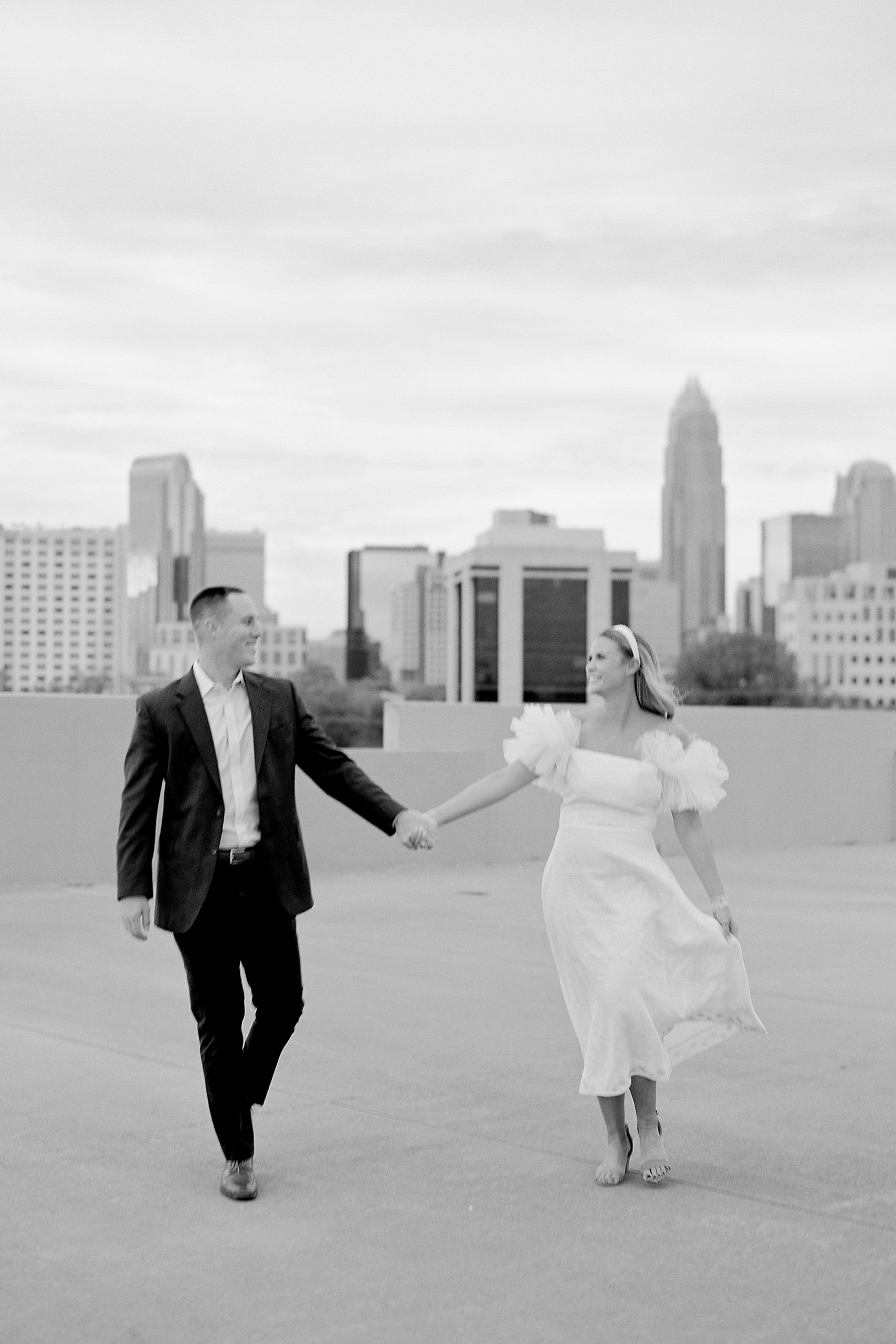 bride and groom hold hands walking in font of Charlotte skyline