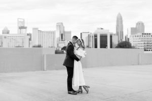 bride and groom stand together with Charlotte skyline behind them