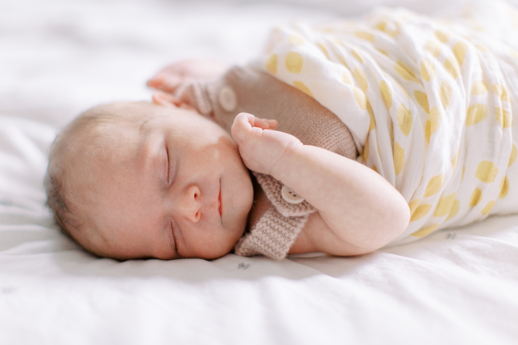 baby lays on bed in yellow and white swaddle