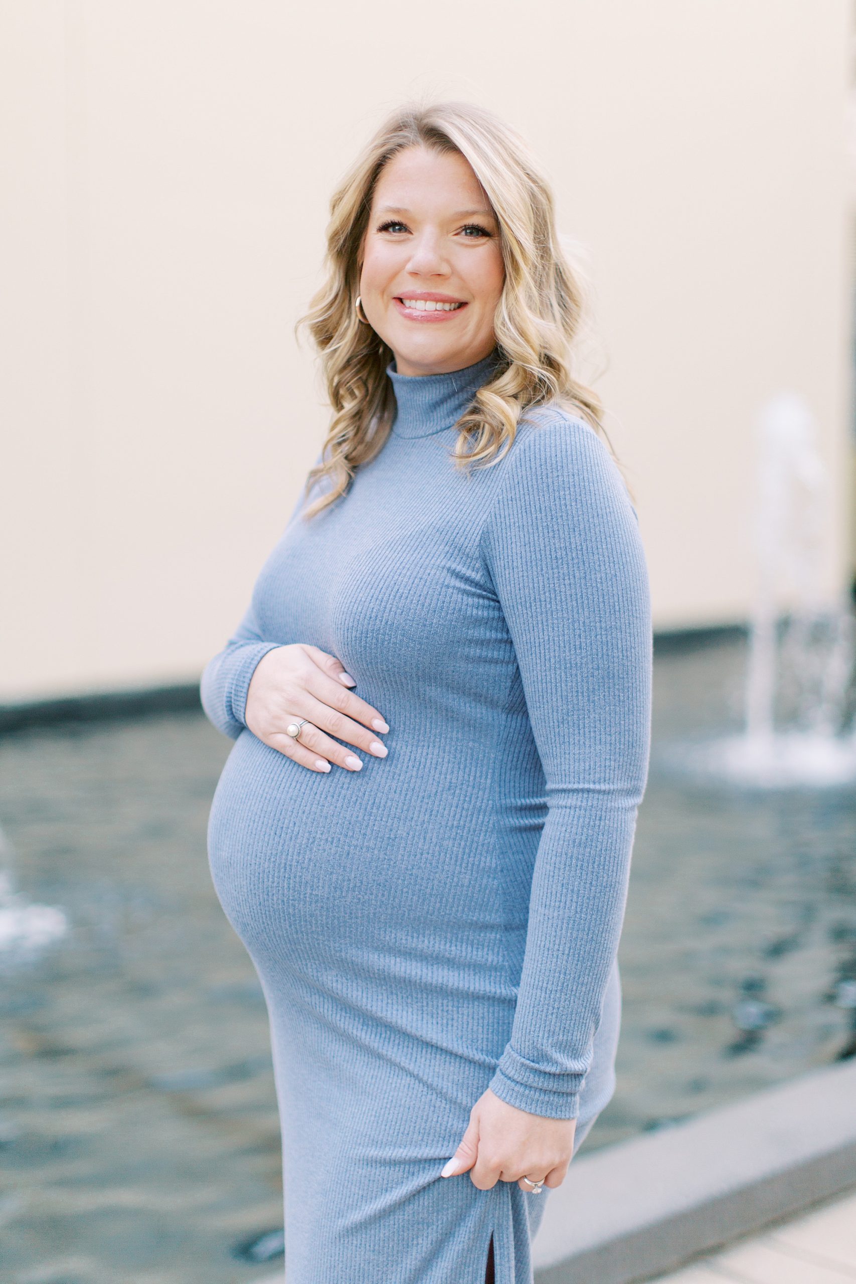 expecting mom holds top of belly in blue sweater dress during maternity photos