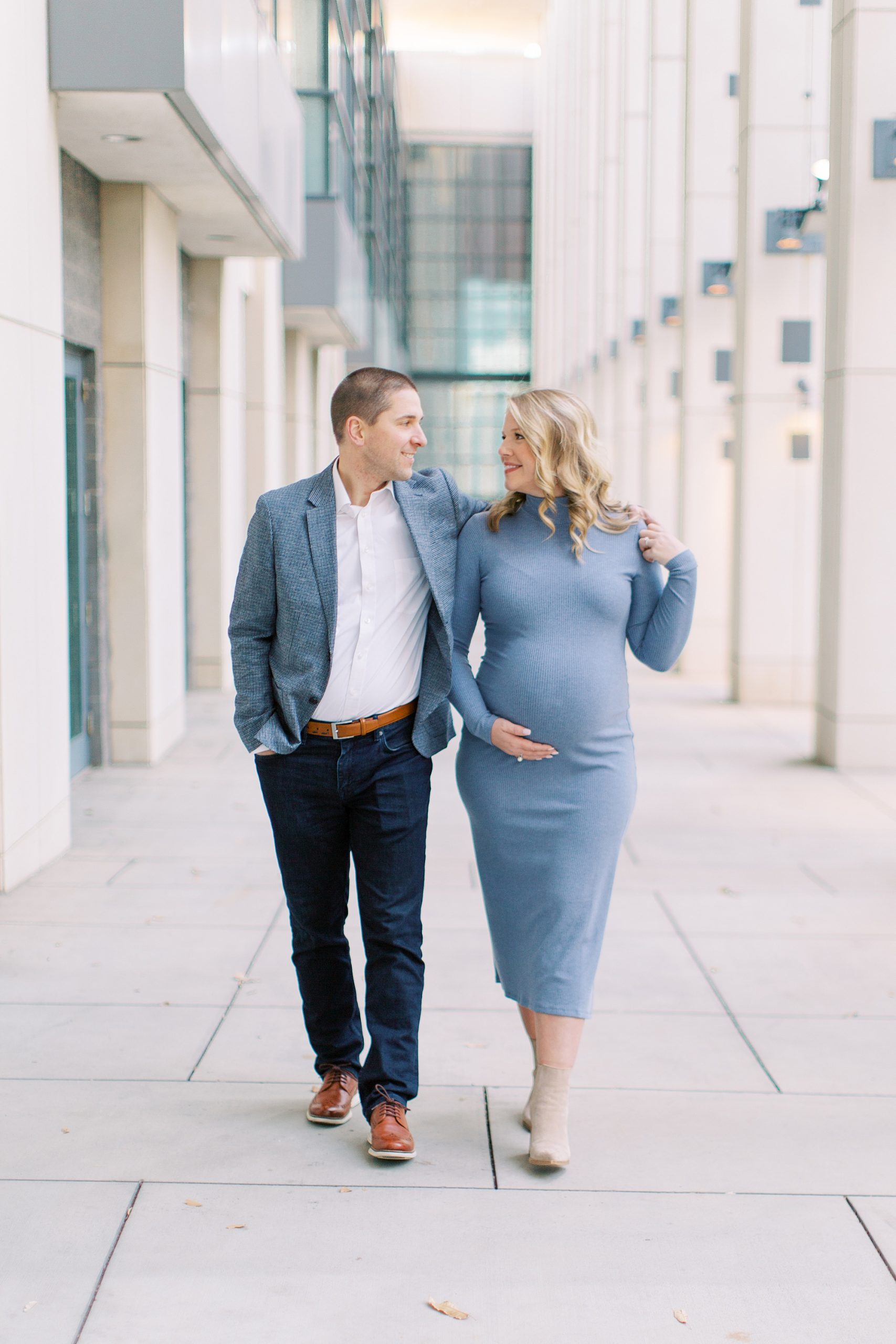 couple walks while woman holds belly during maternity photos in Charlotte NC