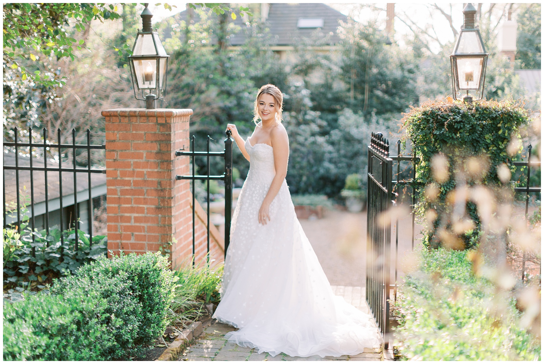 bride stands by wrought iron gate at Duke Mansion in strapless wedding gown 
