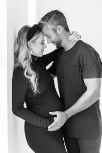 husband and wife lean together against wall during studio maternity session