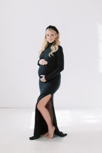 woman stands in black gown with black headband during studio maternity session