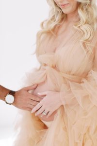 man holds wife's belly in peach maternity gown