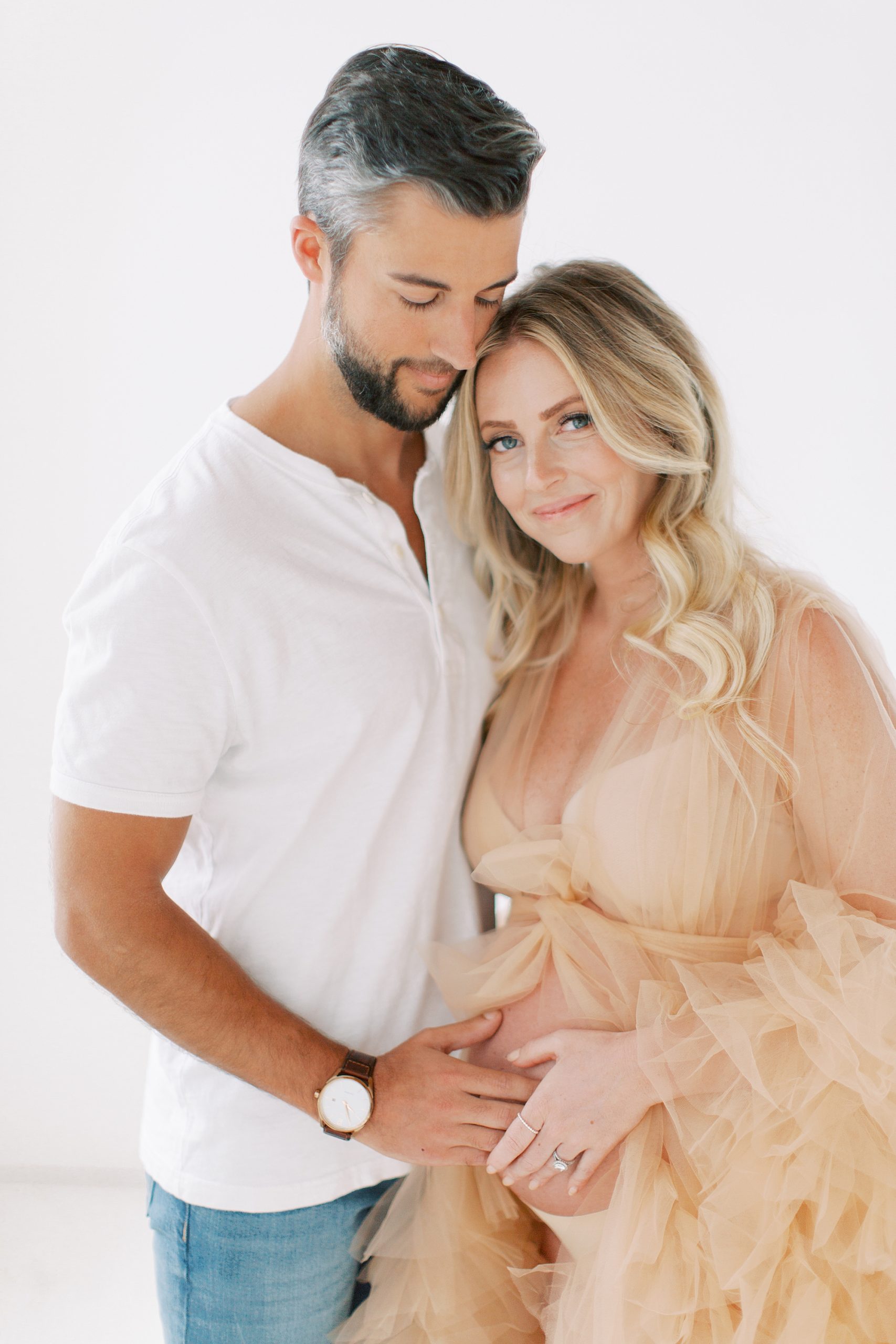 woman in chic peach gown hugs husband during maternity shoot