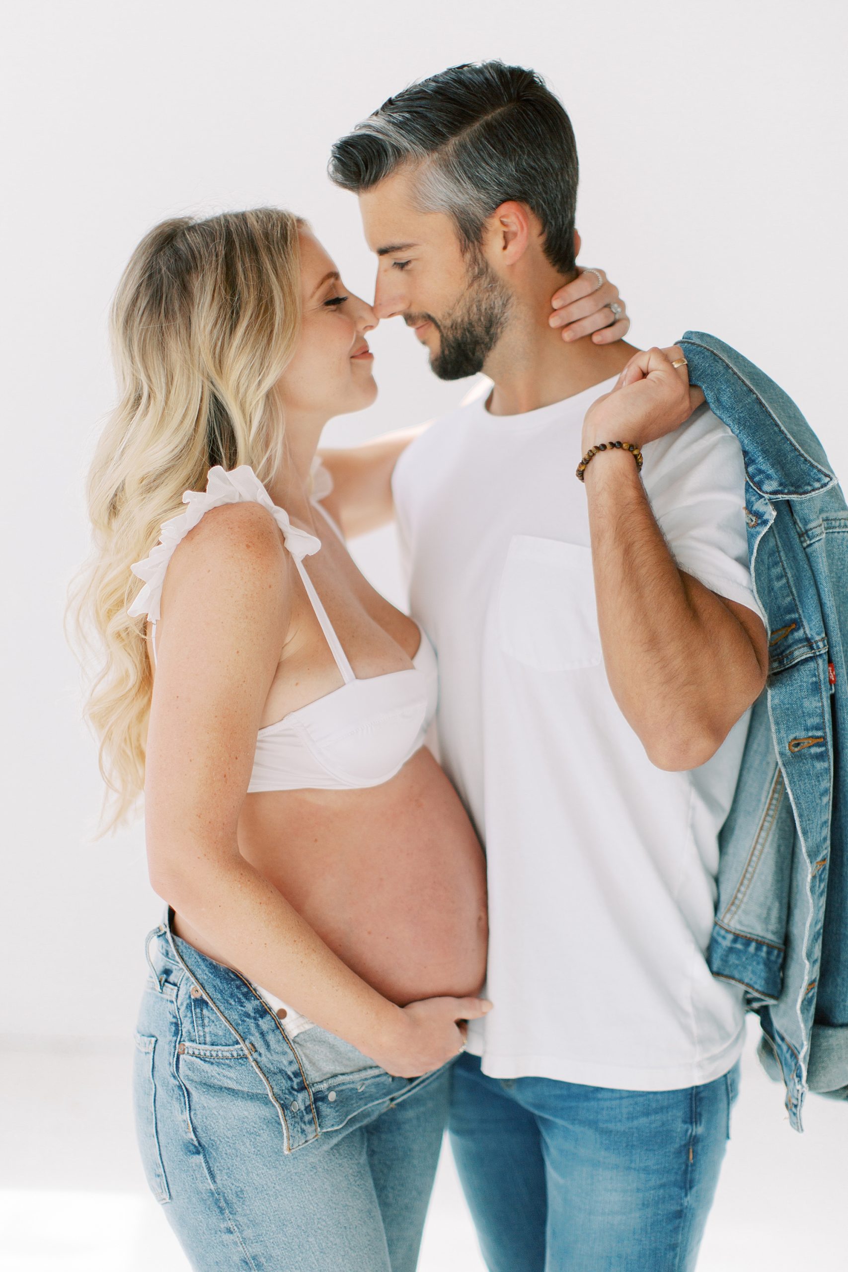 couple stands with noses touching during fashion inspired studio maternity session
