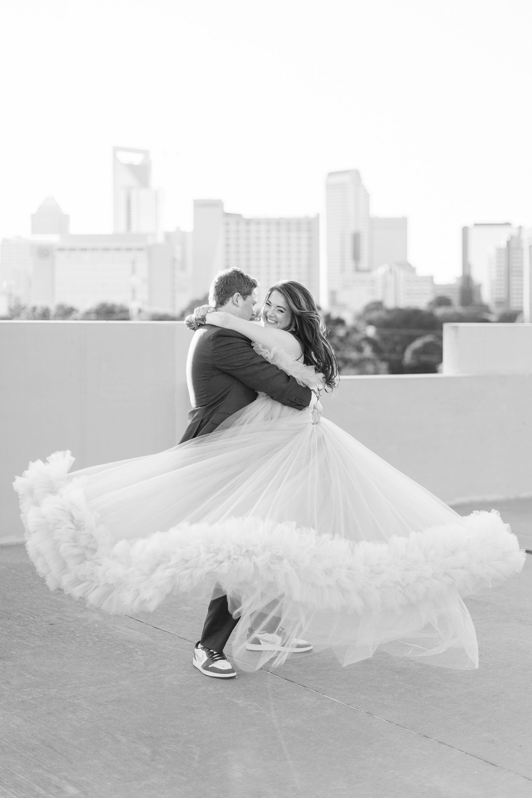 groom twirls bride around showing off skirt of dress during glam Charlotte engagement session