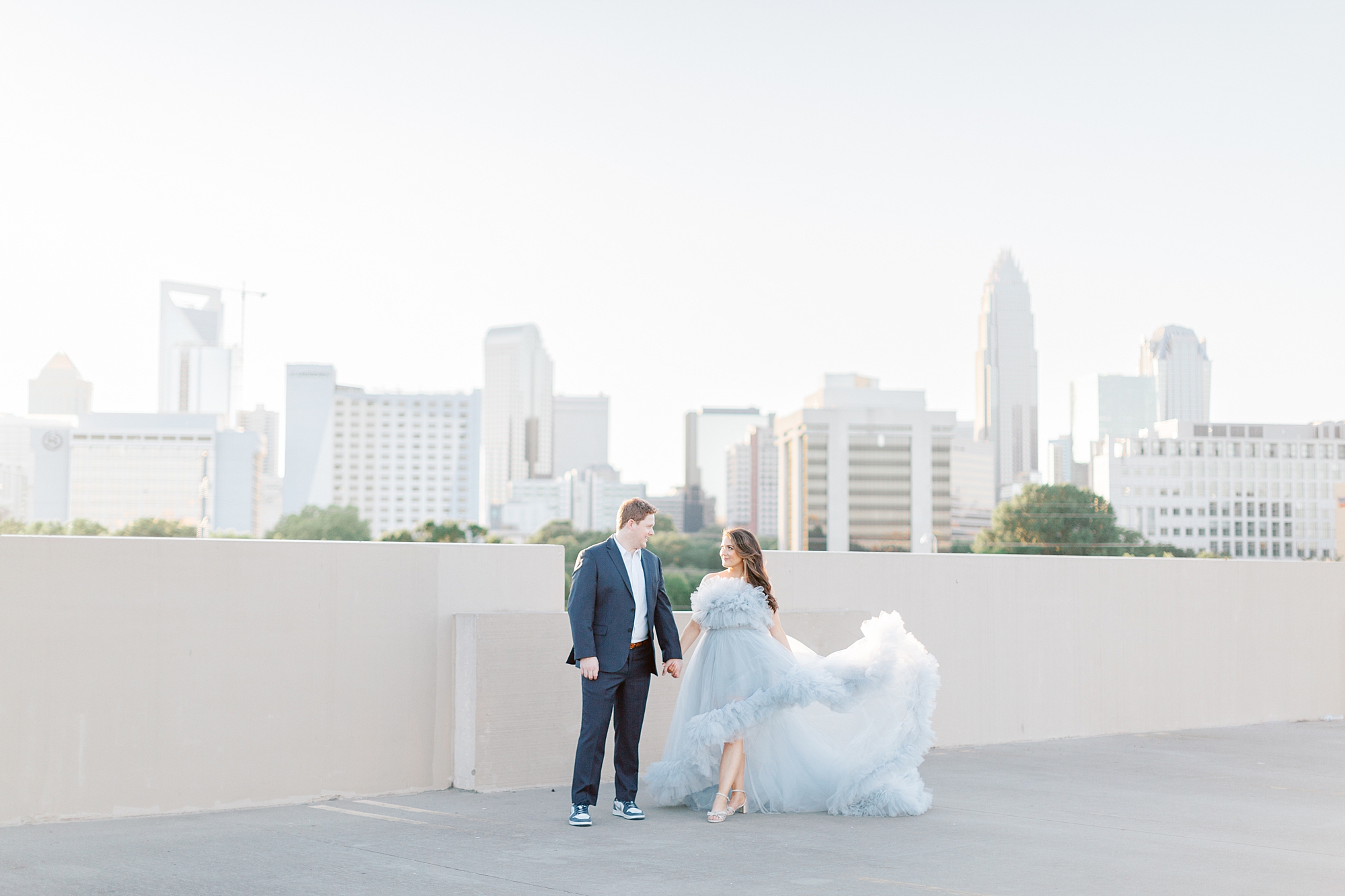 bride and groom hold hands with Charlotte skyline behind them