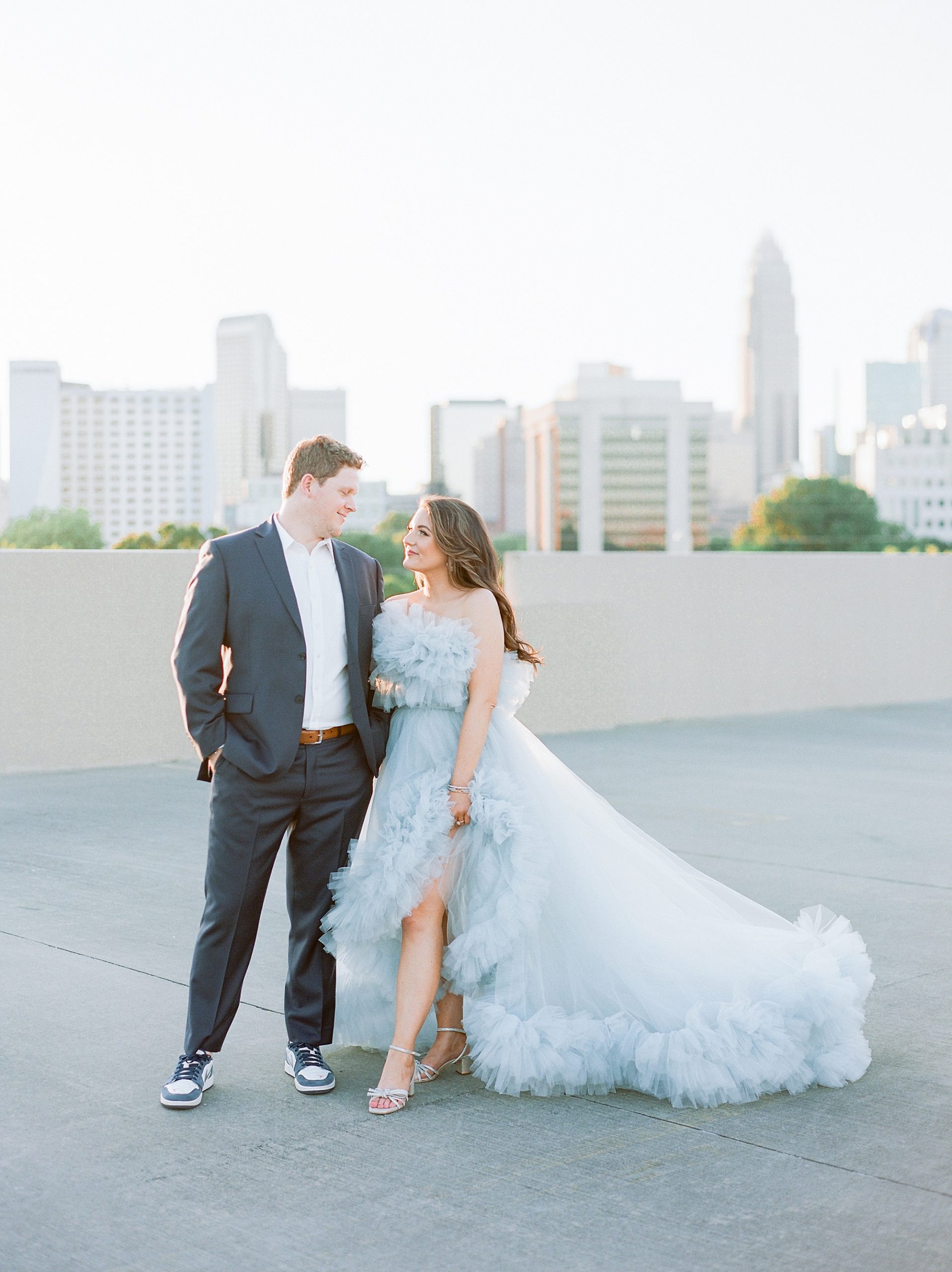 bride leans into groom during glam Charlotte engagement session on rooftop